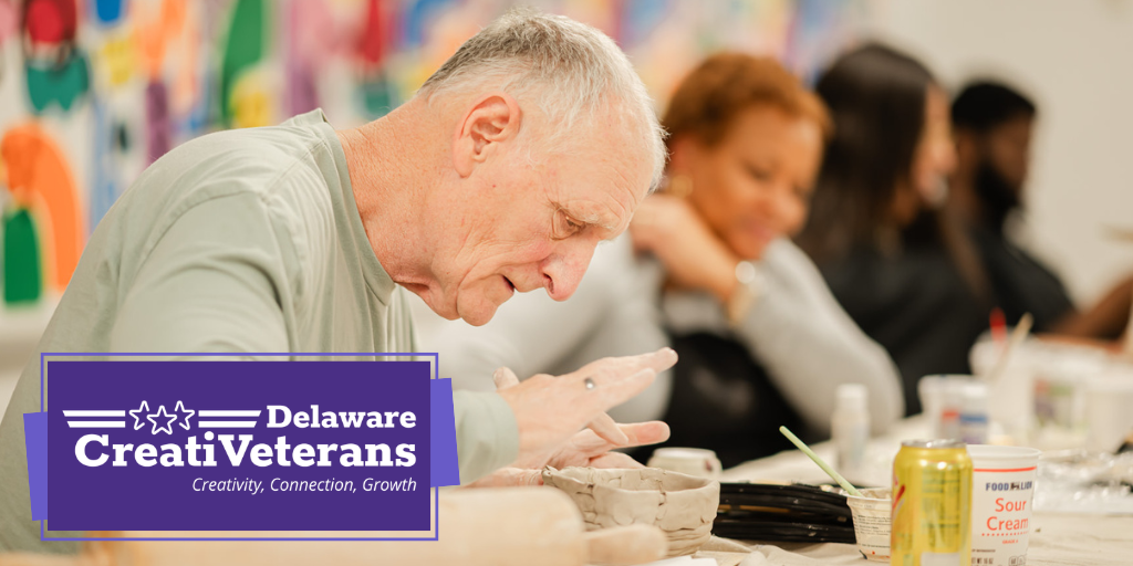 CreatiVeterans logo displayed over a photo of an older veteran sitting at a table with others working with on a clay art piece.